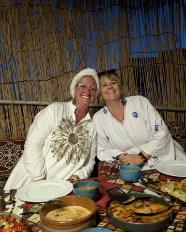 Zwei Frauen sitzen lächelnd an einem Tisch mit traditionellen Speisen.